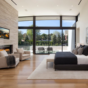 Geräumiges Modernes Hauptschlafzimmer mit Gaskamin, Kaminumrandung aus Stein, weißer Wandfarbe, hellem Holzboden und braunem Boden in Los Angeles