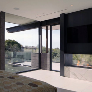 Imagen de dormitorio de estilo americano, grande, con paredes blancas, suelo de baldosas de porcelana, chimenea de doble cara, marco de chimenea de metal y suelo blanco