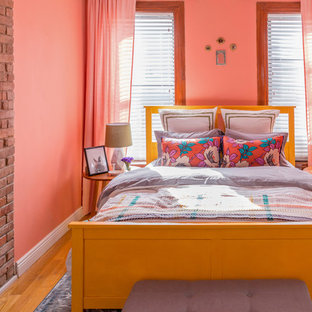 Modelo de dormitorio ecléctico con parades naranjas, suelo de madera en tonos medios, chimenea tradicional y marco de chimenea de ladrillo