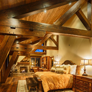 Diseño de dormitorio principal, rústico, de tamaño medio, con suelo de madera oscura, chimenea tradicional y marco de chimenea de piedra