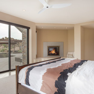 Diseño de dormitorio principal, contemporáneo, grande, con paredes beige, suelo de piedra caliza, chimenea de esquina y marco de chimenea de piedra