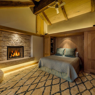 Diseño de dormitorio principal, rural, grande, con paredes beige, suelo de madera clara, chimenea tradicional y marco de chimenea de piedra