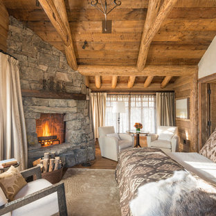 Immagine di una camera matrimoniale stile rurale con pavimento in legno massello medio, cornice del camino in pietra e camino ad angolo
