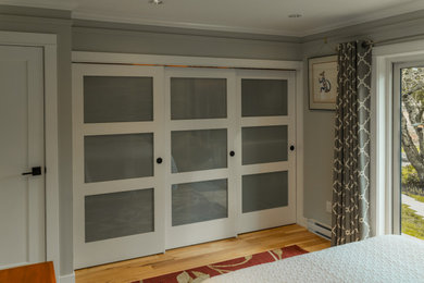 他の地域にある中くらいなトランジショナルスタイルのおしゃれな主寝室 (グレーの壁、無垢フローリング、茶色い床)