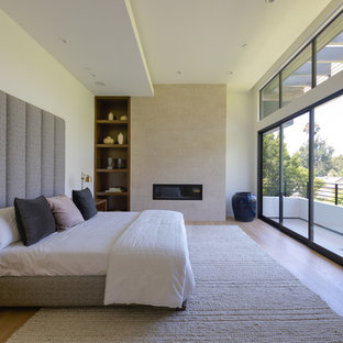 Modelo de dormitorio moderno con paredes blancas, suelo de madera en tonos medios, chimenea lineal, marco de chimenea de baldosas y/o azulejos y suelo marrón