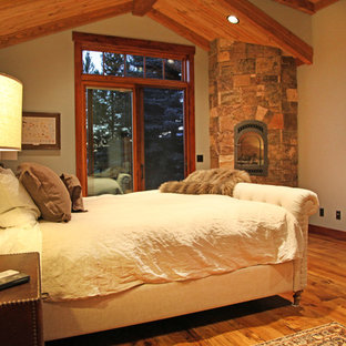 Foto de dormitorio principal, rural, con suelo de madera clara, chimenea de esquina y marco de chimenea de piedra