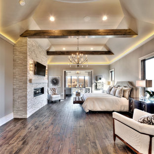 Geräumiges Modernes Hauptschlafzimmer mit grauer Wandfarbe, braunem Holzboden, Gaskamin und Kaminumrandung aus Stein in Kansas City