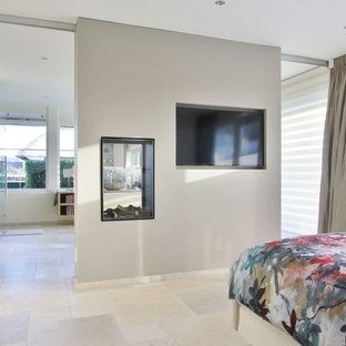 Foto de dormitorio principal, contemporáneo, con paredes beige, suelo de piedra caliza y chimenea de doble cara