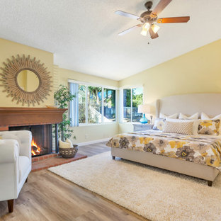 Klassisches Schlafzimmer mit gelber Wandfarbe, braunem Holzboden, Kamin, braunem Boden und gewölbter Decke in Los Angeles