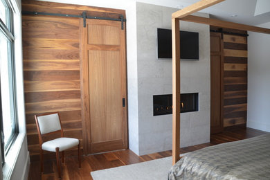 Foto de dormitorio principal actual con paredes blancas, suelo de madera en tonos medios, todas las chimeneas y marco de chimenea de piedra