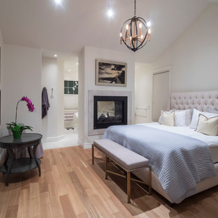 Modelo de dormitorio principal, tradicional renovado, de tamaño medio, con paredes blancas, suelo de madera clara, chimenea de doble cara y marco de chimenea de baldosas y/o azulejos