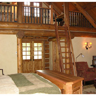 Imagen de dormitorio principal, rústico, grande, con paredes beige, suelo de madera oscura, chimenea de doble cara y marco de chimenea de piedra