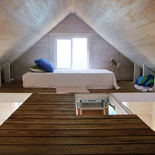 Modelo de dormitorio tipo loft, costero, pequeño, con paredes beige y suelo de madera en tonos medios