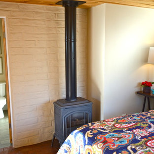 Diseño de dormitorio principal, de estilo americano, de tamaño medio, con paredes blancas, suelo de ladrillo y estufa de leña