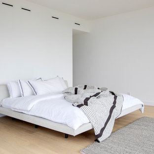 Großes Modernes Hauptschlafzimmer mit weißer Wandfarbe, hellem Holzboden, Hängekamin, Kaminumrandung aus Metall und beigem Boden in Vancouver
