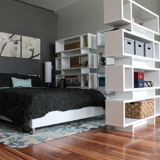 Imagen de dormitorio tipo loft, industrial, con paredes grises y suelo de madera en tonos medios