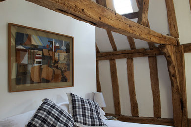 Ejemplo de dormitorio principal de estilo de casa de campo de tamaño medio con paredes blancas, suelo de madera en tonos medios y techo inclinado
