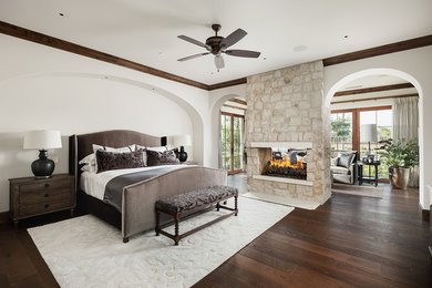 Inspiration for a mediterranean master dark wood floor bedroom remodel in Phoenix with white walls, a two-sided fireplace and a stone fireplace
