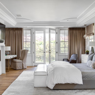 Idée de décoration pour une grand chambre parentale méditerranéenne avec un mur blanc, un sol en bois brun, une cheminée standard, un manteau de cheminée en carrelage et un sol beige.