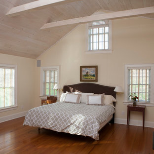 Modelo de dormitorio principal, campestre, grande, con paredes beige, suelo de madera en tonos medios, chimenea tradicional y marco de chimenea de madera