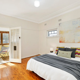 Photo of a large midcentury guest bedroom in Sydney with beige walls, medium hardwood floors, brown floor and no fireplace.