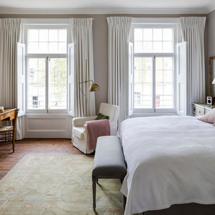 Traditional master bedroom in London with grey walls, a stone fireplace surround, medium hardwood flooring, a standard fireplace and brown floors.