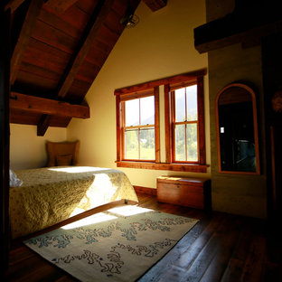 Ejemplo de dormitorio tipo loft, rural, grande, con paredes amarillas, suelo de madera en tonos medios, chimenea tradicional, marco de chimenea de hormigón y suelo marrón