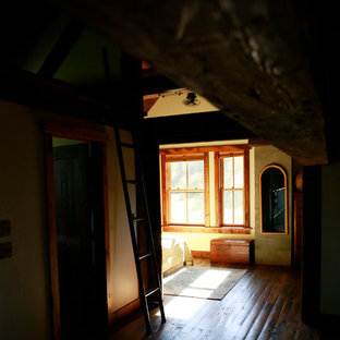 Foto de dormitorio tipo loft, rústico, grande, con paredes amarillas, suelo de madera en tonos medios, chimenea tradicional y marco de chimenea de hormigón