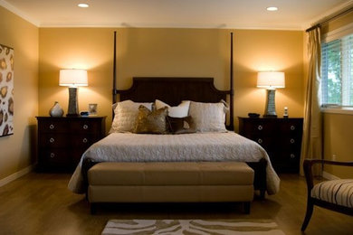 Modelo de dormitorio principal clásico de tamaño medio con paredes amarillas y suelo de madera en tonos medios