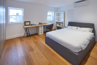 Cette photo montre une chambre d'amis tendance de taille moyenne avec un mur blanc, parquet clair, aucune cheminée et un sol marron.