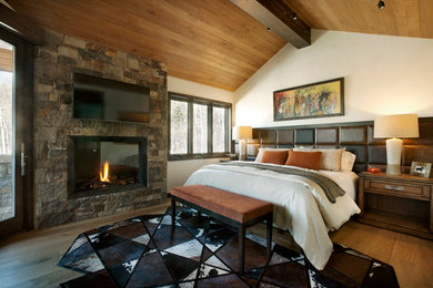 Mountain style master medium tone wood floor bedroom photo in Denver with a standard fireplace, a stone fireplace and white walls