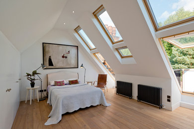 Photo of a contemporary loft bedroom in London with white walls, medium hardwood flooring and no fireplace.