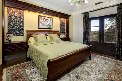 Ejemplo de dormitorio principal clásico de tamaño medio sin chimenea con paredes amarillas y suelo de madera oscura