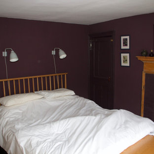 Modelo de dormitorio principal, de estilo americano, grande, con paredes púrpuras, suelo de madera oscura, chimenea tradicional, marco de chimenea de ladrillo y suelo marrón