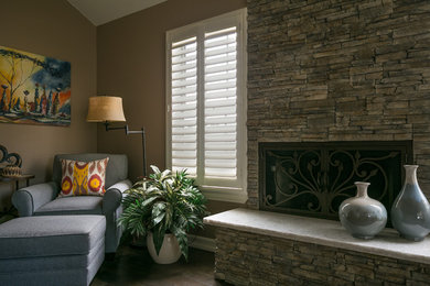 Exemple d'une grande chambre d'amis montagne avec un mur gris, un sol en carrelage de porcelaine, une cheminée standard, un manteau de cheminée en pierre et un sol marron.