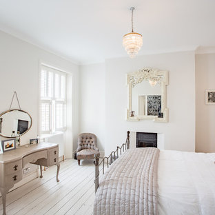 Immagine di una camera da letto chic di medie dimensioni con pareti grigie, pavimento in legno verniciato, camino classico, cornice del camino in intonaco e pavimento bianco