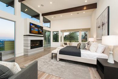 Großes Modernes Hauptschlafzimmer mit weißer Wandfarbe, hellem Holzboden, Gaskamin, gefliester Kaminumrandung und braunem Boden in Los Angeles