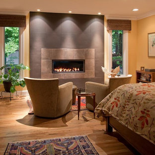 Modelo de dormitorio principal, clásico renovado, grande, con paredes amarillas, suelo de madera en tonos medios, chimenea lineal y marco de chimenea de baldosas y/o azulejos