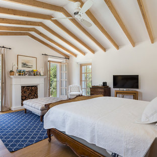 Imagen de dormitorio principal, mediterráneo, con paredes blancas, suelo de madera en tonos medios, chimenea tradicional y suelo marrón
