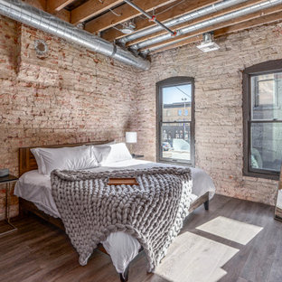 Mittelgroßes Industrial Schlafzimmer ohne Kamin mit braunem Boden, Ziegelwänden und freigelegten Dachbalken in Sonstige