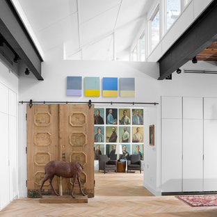 Imagen de dormitorio principal, industrial, grande, con paredes blancas, suelo de madera clara y chimenea lineal