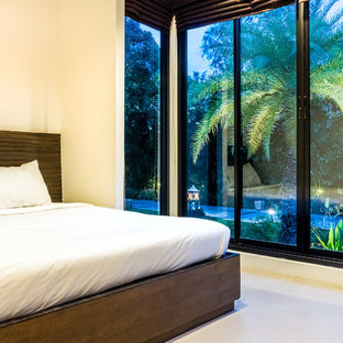 Imagen de dormitorio principal, tropical, de tamaño medio, sin chimenea, con paredes amarillas, suelo de cemento y suelo gris