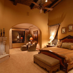 Modelo de dormitorio principal, clásico, extra grande, con paredes amarillas, moqueta, chimenea tradicional, marco de chimenea de yeso y suelo beige