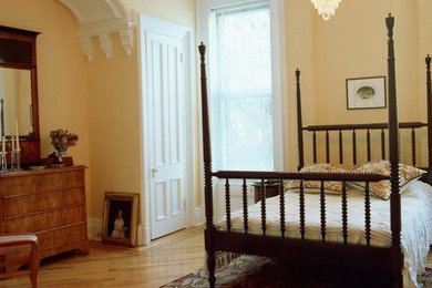 Modelo de dormitorio principal sin chimenea con paredes amarillas y suelo de madera clara