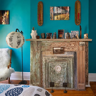 Mittelgroßes Eklektisches Hauptschlafzimmer mit blauer Wandfarbe, braunem Holzboden, Hängekamin und Kaminumrandung aus Metall in New York