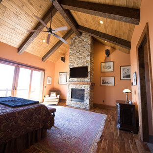 Imagen de dormitorio principal, rural, grande, con parades naranjas, suelo de madera en tonos medios y marco de chimenea de piedra