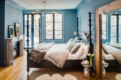 Ejemplo de dormitorio bohemio con paredes azules, suelo de madera en tonos medios, todas las chimeneas y marco de chimenea de piedra