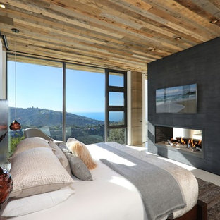 Diseño de dormitorio principal, actual, grande, con paredes beige, suelo de baldosas de porcelana, chimenea de doble cara, marco de chimenea de yeso y suelo beige