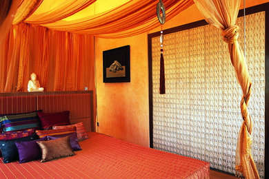 他の地域にある中くらいなエクレクティックスタイルのおしゃれな主寝室 (オレンジの壁、淡色無垢フローリング)