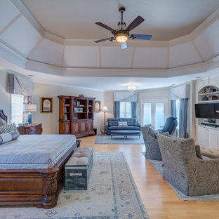 Imagen de dormitorio principal, tradicional renovado, grande, con paredes grises, suelo de madera clara, chimenea tradicional y marco de chimenea de madera